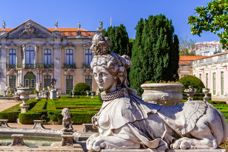 Queluz, Portugal. Sphinx sculpture at the Neptune gardens and Cerimonial Facade on the Queluz Royal Palace. Formerly used as the Summer residence by the Portuguese royal family.