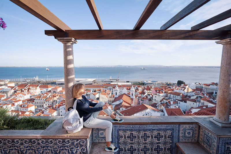 Traveling by Portugal. Young traveling woman enjoying old town Lisbon view, red tiled roofs, ancient architecture and river.